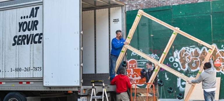 Four people carrying a wooden construction into a moving truck