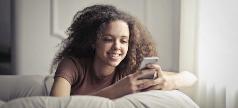 Photo of Smiling Woman Sitting on a Gray Bean Bag While Using Her Phone and booking last minute movers Philadelphia residents rely on